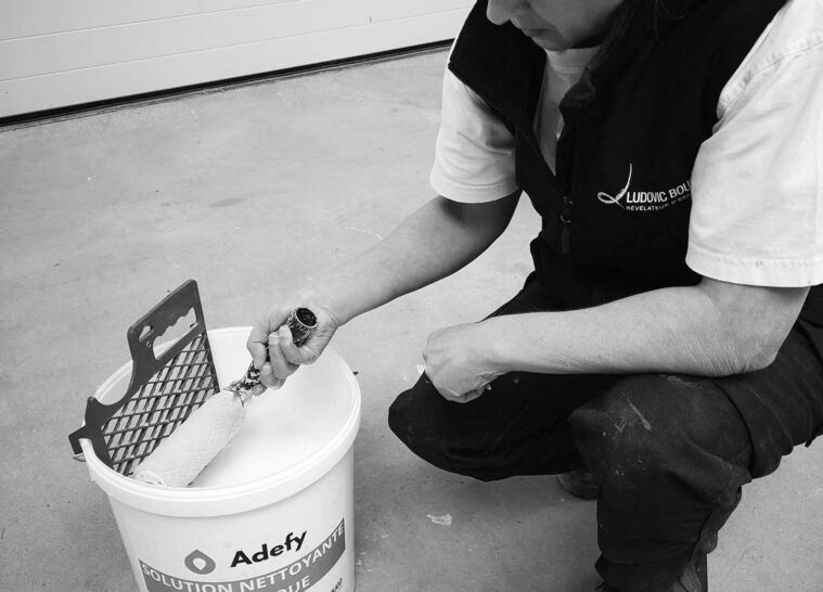 Une employée de Ludovic Bougo en tenue de travail, avec un sceau et un rouleau de peinture.